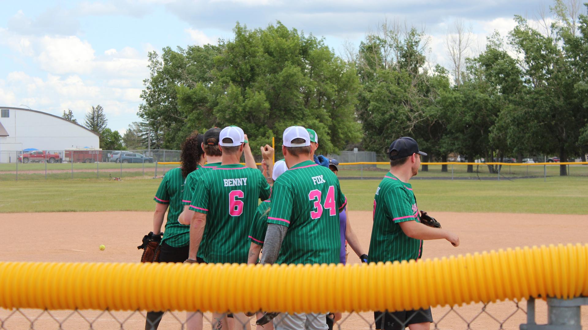 Team wearing green jerseys with pink numbers huddle after a play.