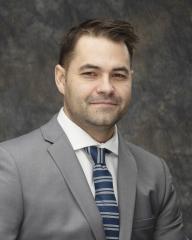 Headshot of town councillor Cole Dunham, a white man with dark hair and a grey suit with a blue tie. 