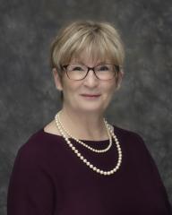 Headshot of town councillor Judy Sanderson, a white woman with blonde hair, a dark shirt, and a string of pearls. 