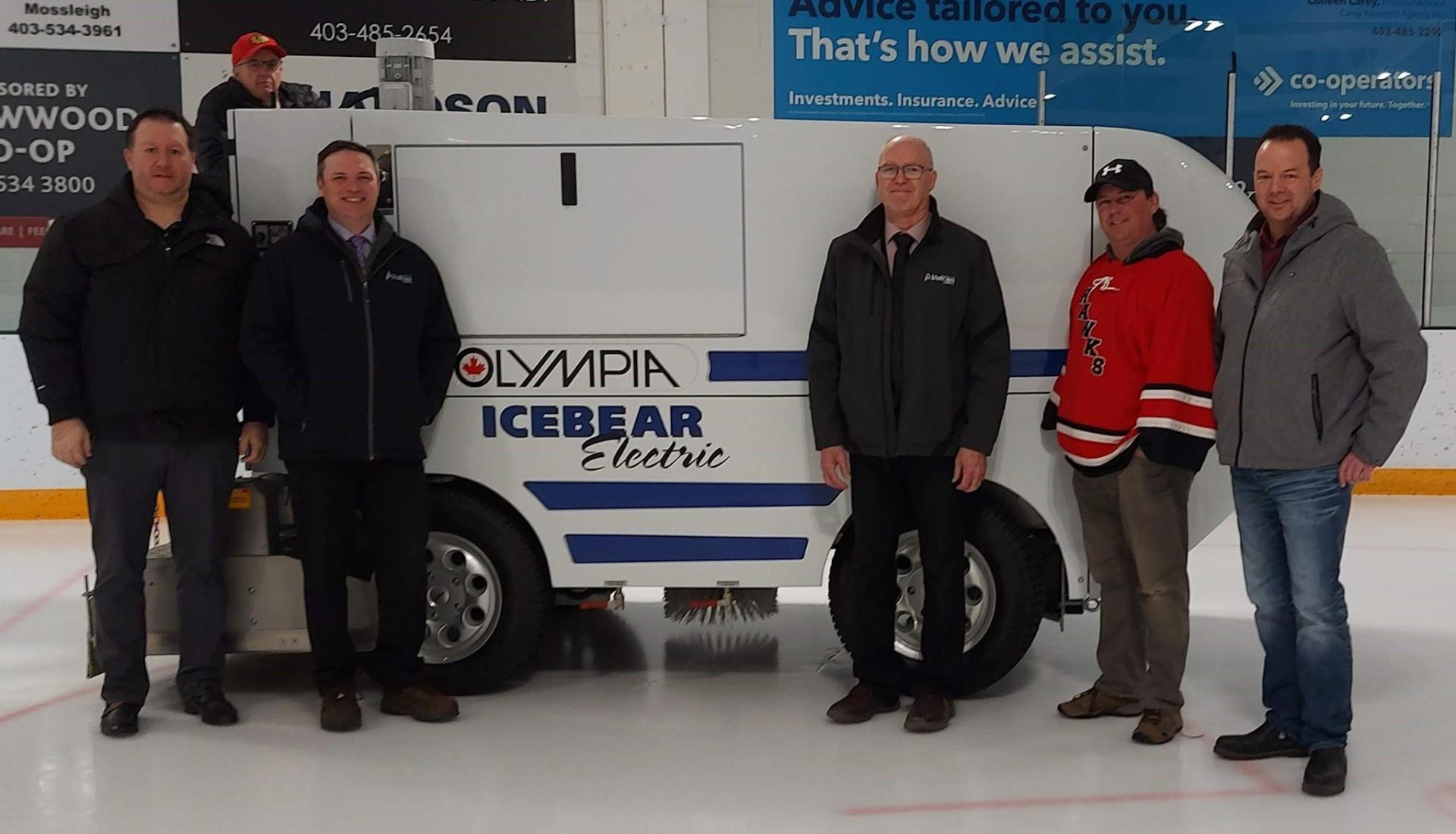 Group of people standing in front of new ice resurfacer machine.